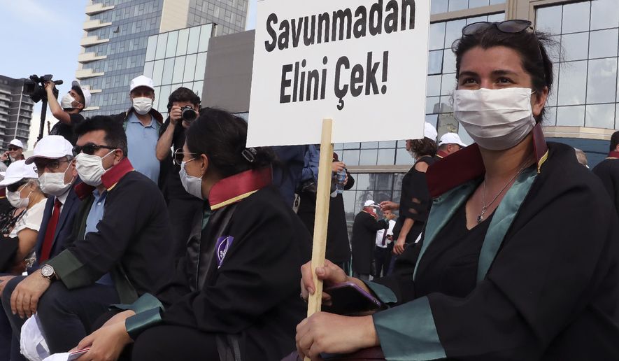 Lawyers wearing face masks to protect against the spread of coronavirus, as one holds a placard that reads "Don't touch the Defence!" during a protest, in Ankara, Turkey, Monday, June 22, 2020. Turkish authorities have made the wearing of masks mandatory in three major cities to curb the spread of COVID-19 following an uptick in confirmed cases since the reopening of many businesses. (AP Photo/Burhan Ozbilici)
