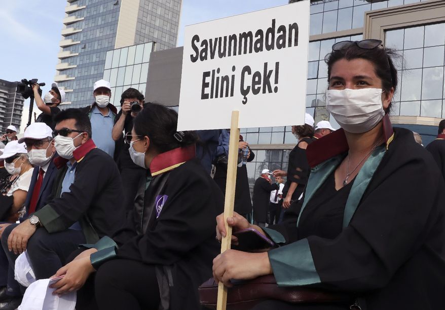 Lawyers wearing face masks to protect against the spread of coronavirus, as one holds a placard that reads "Don't touch the Defence!" during a protest, in Ankara, Turkey, Monday, June 22, 2020. Turkish authorities have made the wearing of masks mandatory in three major cities to curb the spread of COVID-19 following an uptick in confirmed cases since the reopening of many businesses. (AP Photo/Burhan Ozbilici)