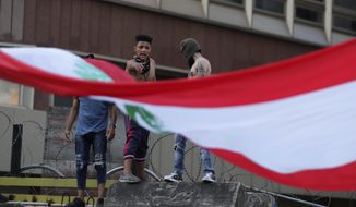 Anti-government protesters stand on a concrete wall that installed by authorities to block a road leading to the parliament building and shout slogans during ongoing protests against the Lebanese government in Beirut, Lebanon, Sunday, June 14, 2020. (AP Photo/Hassan Ammar)