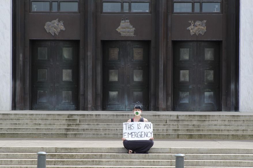 In this Tuesday, June 23, 2020, a lone masked protester sits in front of the Oregon State Capitol in Salem, Ore. Starting Wednesday lawmakers will be meeting in a special session to deal mainly with the coronavirus pandemic and police brutality. (AP Photo/Andrew Selsky)