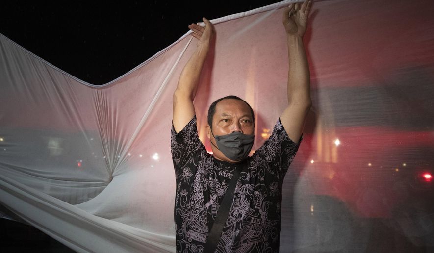 An anti-government activist tries to set up a shite sheet to project a video in Bangkok, Thailand, Wednesday, June 24, 2020. Anti-government activists in the Thai capital Bangkok on Wednesday held a pre-dawn commemoration of a military coup that installed constitutional rule almost nine decades ago, defying official warnings and police harassment. (AP Photo/Sakchai Lalit)