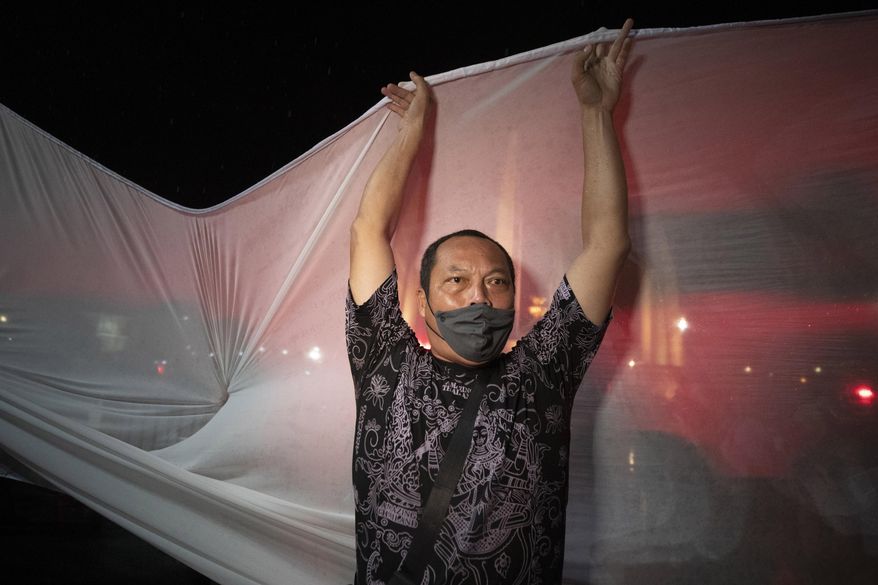 An anti-government activist tries to set up a shite sheet to project a video in Bangkok, Thailand, Wednesday, June 24, 2020. Anti-government activists in the Thai capital Bangkok on Wednesday held a pre-dawn commemoration of a military coup that installed constitutional rule almost nine decades ago, defying official warnings and police harassment. (AP Photo/Sakchai Lalit)