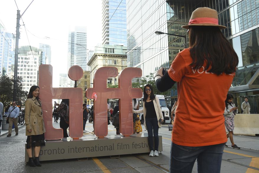 FILE - In this Sept. 5, 2019 file photo, a volunteer takes a photo of people next to signage promoting the Toronto International Film Festival in Toronto. The festival, one of the leading launching pads for fall movies and Oscar contenders, announced plans for a smaller 2020 edition with virtual red carpet premieres and drive-in screenings. It is typically a sprawling city-wide affair that hosts between 250-400 feature-length films and the debuts of many of the fall movie season’s top releases. (Photo by Chris Pizzello/Invision/AP, File)