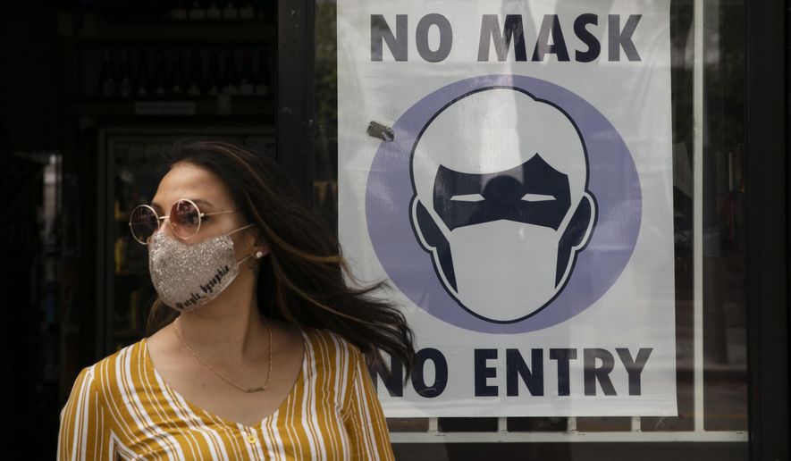 A woman walks out of a liquor store past a sign requesting its customers to wear a mask Tuesday, June 23, 2020, in Santa Monica, Calif. The state Department of Public Health recorded more than 5,000 new cases Tuesday, putting the total number of positive cases at more than 183,000. The state has seen more than 5,500 deaths related to COVID-19. (AP Photo/Jae C. Hong)