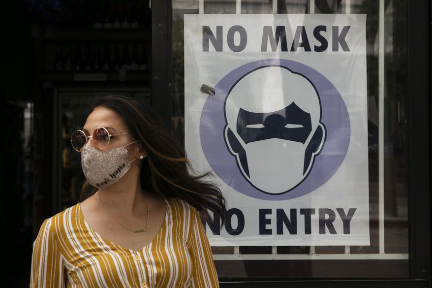 A woman walks out of a liquor store past a sign requesting its customers to wear a mask Tuesday, June 23, 2020, in Santa Monica, Calif. The state Department of Public Health recorded more than 5,000 new cases Tuesday, putting the total number of positive cases at more than 183,000. The state has seen more than 5,500 deaths related to COVID-19. (AP Photo/Jae C. Hong)