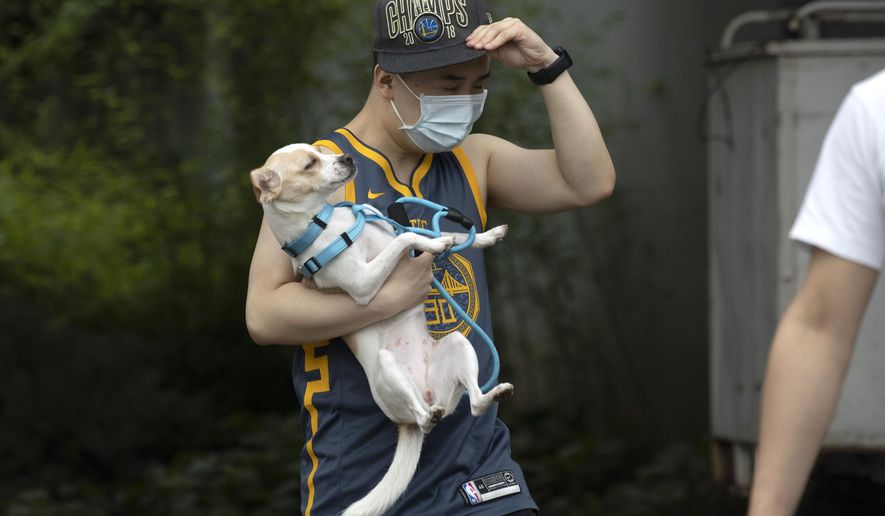 A man wearing a mask carries his dog along a street in Beijing on Thursday, June 25, 2020. In China, where the virus first appeared late last year, an outbreak in Beijing appeared to have been brought under control. China reporting more than a dozen of newly confirmed cases nationwide amid mass testing in the capital. (AP Photo/Ng Han Guan)