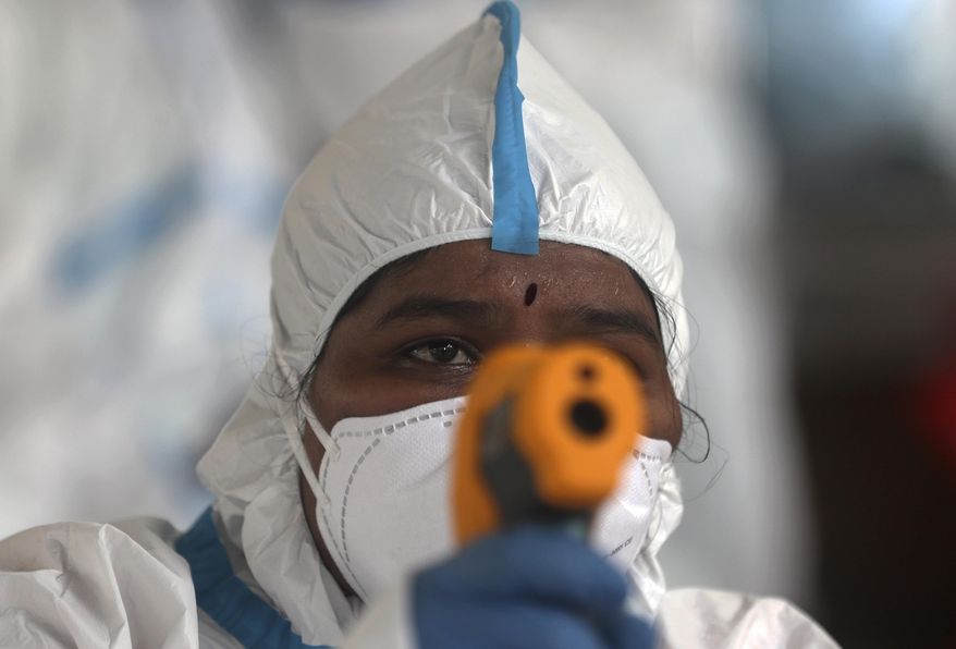 A health worker checks the temperature of a woman during a free medical camp in Dharavi, one of Asia's biggest slums, in Mumbai, India, Friday, June 26, 2020. India is the fourth hardest-hit country by the pandemic in the world after the U.S., Russia and Brazil. (AP Photo/Rafiq Maqbool)