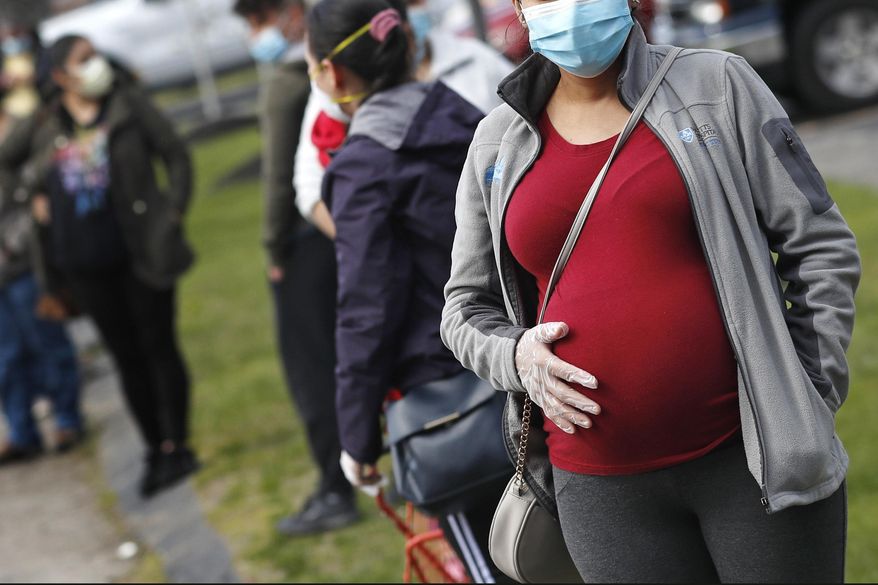 A pregnant woman holds her belly as she waits in line for groceries with hundreds during a food pantry, sponsored by Healthy Waltham for those in need due to the COVID-19 virus outbreak, at St. Mary's Church in Waltham, Mass., Thursday, May 7, 2020. In the past month more than 7,500 bags of food have been donated to the community. (AP Photo/Charles Krupa)