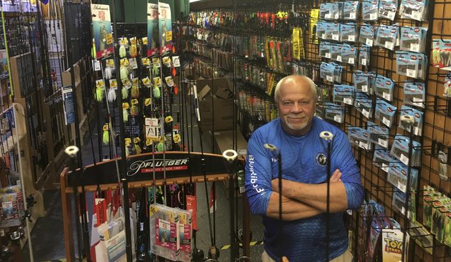 In this Wednesday, June 17, 2020 photo, Dave Becker, a sales associate at Blue Ribbon Bait & Tackle in Oakdale, Minn., poses behind a fishing rod display. Amid the coronavirus outbreak, the store has been nearly selling out its entry-level fishing rods and reels regularly each week before a fresh supply arrives. Fishing activity has skyrocketed during the pandemic. (Dave Orrick/Pioneer Press via AP)