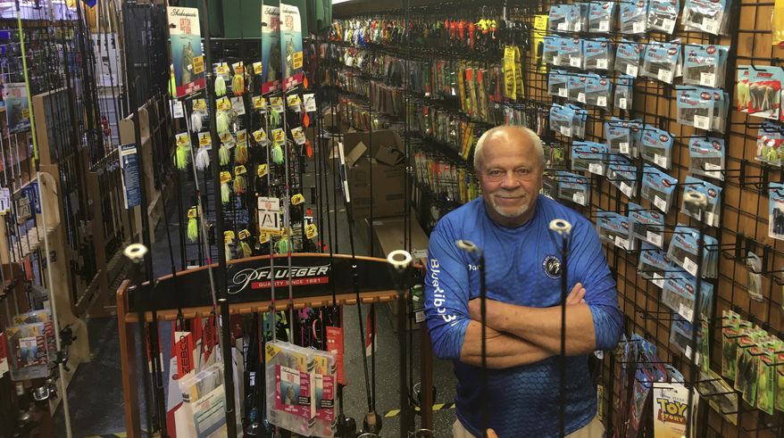 In this Wednesday, June 17, 2020 photo, Dave Becker, a sales associate at Blue Ribbon Bait & Tackle in Oakdale, Minn., poses behind a fishing rod display. Amid the coronavirus outbreak, the store has been nearly selling out its entry-level fishing rods and reels regularly each week before a fresh supply arrives. Fishing activity has skyrocketed during the pandemic. (Dave Orrick/Pioneer Press via AP)