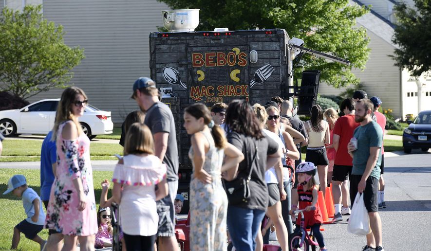 In this Thursday, June 18, 2020, photo, diners line up to patronize Bebo's Mac Shack, a food truck parked on the street in a suburban neighborhood in Eldersburg, Md. Christopher Coil runs Bebo’s Mac Shack with his wife, Katie, out of Westminster Riding Club. His menu is devoted to macaroni and cheese dishes, and the food truck itself is colorful, which Coil said makes them stand out a bit. (Dylan Slagle/The Baltimore Sun via AP)
