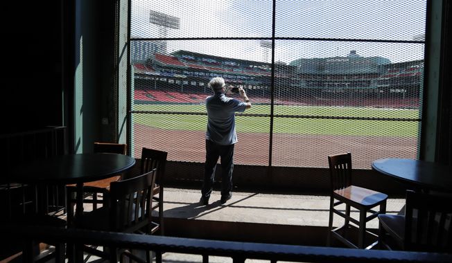 In this June 25, 2020, photo, a reporter photographs the view of the baseball field at Fenway Park from the Bleacher Bar in Boston. Tucked under the center field seats at Fenway Park, down some stairs from Lansdowne Street in an area previously used as the visiting team’s batting cage, is a sports bar that is preparing to reopen from the coronavirus shutdown. If Major League Baseball’s plans remain on schedule, it may be one of the few places fans will be able to watch a game in person this season. (AP Photo/Elise Amendola) ** FILE **