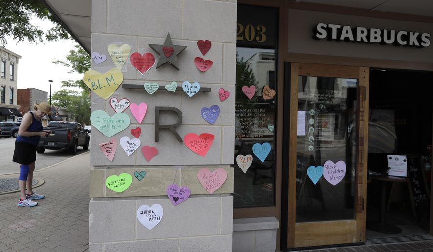 In this Thursday, June 4, 2020, file photo, a woman looks at the plywood covering the windows of a Starbucks store in downtown Naperville, Ill., as Naperville residents used hearts to post messages in support of the Black Lives Matter movement. (AP Photo/Nam Y. Huh, File)