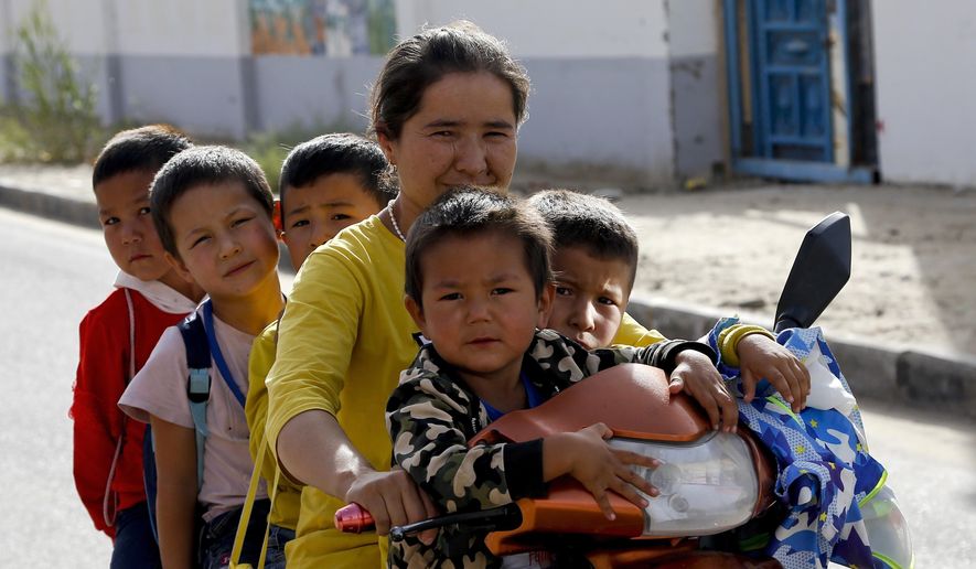 FILE - In this Sept. 20, 2018 file photo, a Uighur woman and children sit on a motor-tricycle after school at the Unity New Village in Hotan, in western China's Xinjiang region. Birth rates in the mostly Uighur regions of Hotan and Kashgar have plunged by more than 60% since 2015, government statistics show. (AP Photo/Andy Wong)