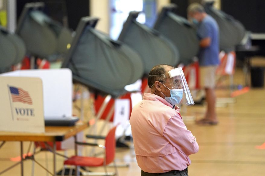 Harris County election clerk Jose Mendoza watches over voting booths, Monday, June 29, 2020, in Houston. Early voting for the Texas primary runoffs began Monday. (AP Photo/David J. Phillip)
