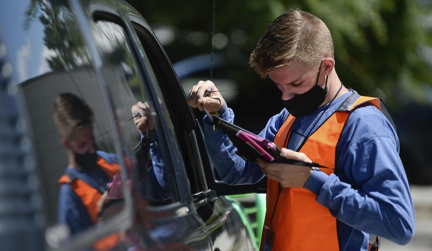 Poll worker Seth Ahlers checks on a voter's registration as people line up at one of 12 drive-up voting assistance centers in Salt Lake County, Utah, Tuesday, June 30, 2020, to get ballots to replace lost ones or get help for unaffiliated voters registering Republican to be able to vote in the primary. Utah was one of a handful of states that decided not to open any in-person polling places this year due to the coronavirus pandemic.(Francisco Kjolseth/The Salt Lake Tribune via AP)