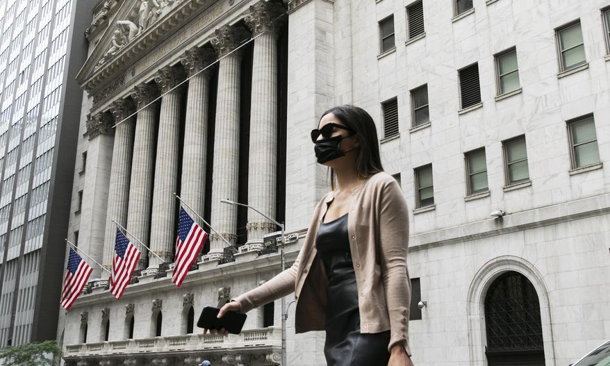 In this file photo, a woman wearing a mask passes the New York Stock Exchange, Tuesday, June 30, 2020, during the coronavirus pandemic. The Congressional Budget Office on July 2, 2020, said it expects a V-shaped economic recovery as the United States rebounds from the coronavirus-related recession. (AP Photo/Mark Lennihan)