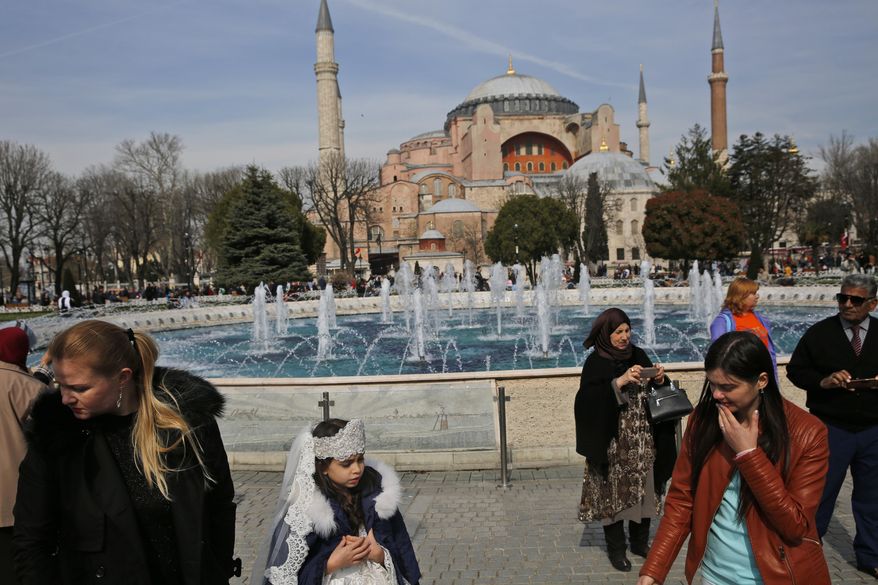 In this Friday, March 24, 2017, file photo, people walk backdropped by the Byzantine-era Hagia Sophia, one of Istanbul&#39;s main tourist attractions, in the historic Sultanahmet district of Istanbul. The 6th-century building is now at the center of a heated debate between conservative groups who want it to be reconverted into a mosque and those who believe the World Heritage site should remain a museum. (AP Photo/Lefteris Pitarakis, File)