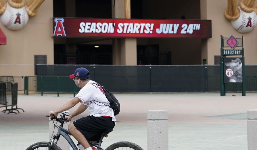 A Los Angeles Angels fan rides a bike past the entrance of Angels Stadium on Wednesday, July 1, 2020, in Anaheim, Calif. The Angels and other Major League Baseball teams will report to their respective facilities for training this week, amid the coronavirus pandemic. (AP Photo/Ashley Landis)