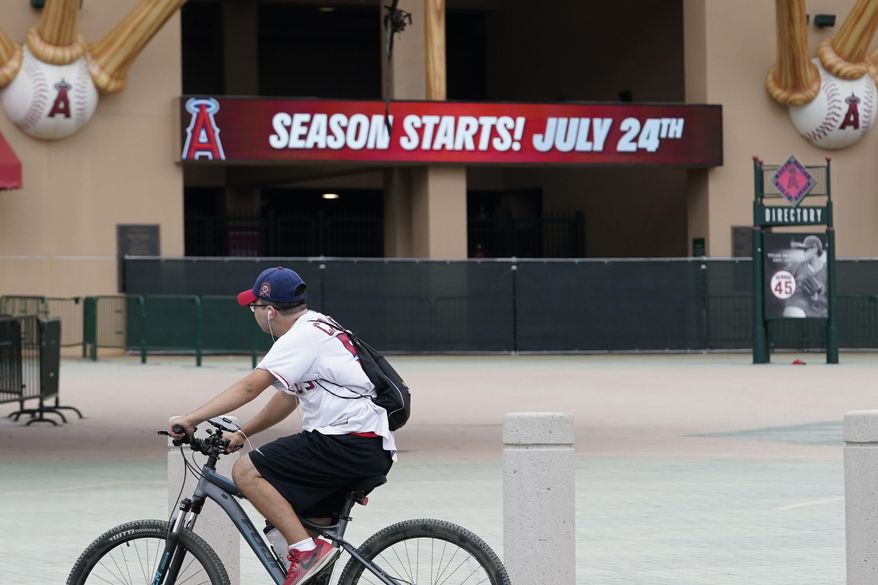 A Los Angeles Angels fan rides a bike past the entrance of Angels Stadium on Wednesday, July 1, 2020, in Anaheim, Calif. The Angels and other Major League Baseball teams will report to their respective facilities for training this week, amid the coronavirus pandemic. (AP Photo/Ashley Landis)