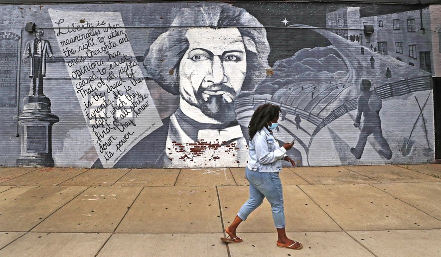 In this Wednesday, June 24, 2020, photograph, a woman walks past a mural in tribute to Frederick Douglass on the exterior wall of the Black-owned Slade&#x27;s Bar and Grill in the South End neighborhood of Boston. Many from outside Boston have recently ordered takeout, purchased gift cards and supported the restaurant amid nationwide protests against racism. (AP Photo/Charles Krupa)