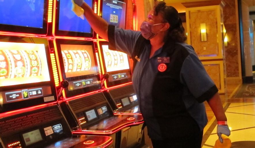 Jeorganna Barnes, a worker at Harrah&#x27;s casino in Atlantic City, N.J., wipes slot machines with disinfectant Wednesday, July 1, 2020, as the casino prepared to reopen after 3 1/2 months of being shut down due to the coronavirus. Five of Atlantic City&#x27;s casinos will reopen on Thursday, while three others, including Harrah&#x27;s, will open Friday. (AP Photo/Wayne Parry)