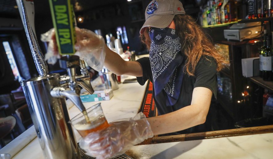 In this June 22, 2020, file photo, a bartender pours a beer for a customer at Shade Bar NYC in New York. Authorities are closing honky tonks, bars and other drinking establishments in some parts of the U.S. to stem the surge of COVID-19 infections — a move backed by sound science about risk factors that go beyond wearing or not wearing masks. (AP Photo/John Minchillo, File)