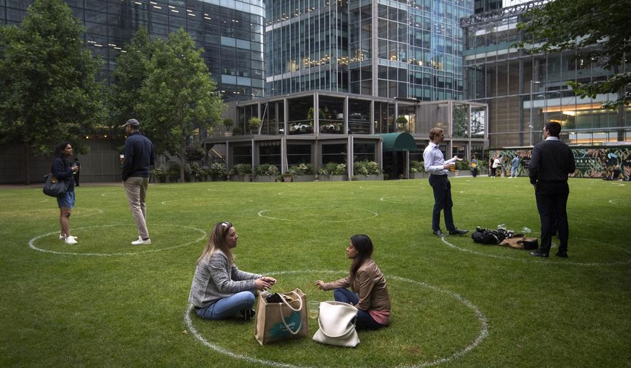 Drinkers stand within rings marked on the grass to maintain their social distance outside a bar in Canary Wharf, East London as further coronavirus lockdown restrictions are lifted in England, on Wednesday, July 1, 2020. (Victoria Jones/PA via AP)
