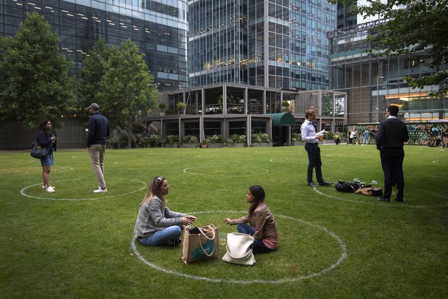 Drinkers stand within rings marked on the grass to maintain their social distance outside a bar in Canary Wharf, East London as further coronavirus lockdown restrictions are lifted in England, on Wednesday, July 1, 2020. (Victoria Jones/PA via AP)
