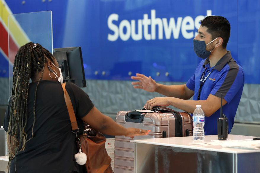 FILE - In this Wednesday, June 24, 2020, file photo, Southwest airlines employee Oscar Gonzalez, right, assists a passenger at the ticket counter at Love Field in Dallas. In a report, Thursday, July 2, 2020, the government is recommending that travelers wear face coverings during air travel and says airlines should consider limiting capacity on planes to promote social distancing. But it stopped short of making new requirements. (AP Photo/Tony Gutierrez, File)