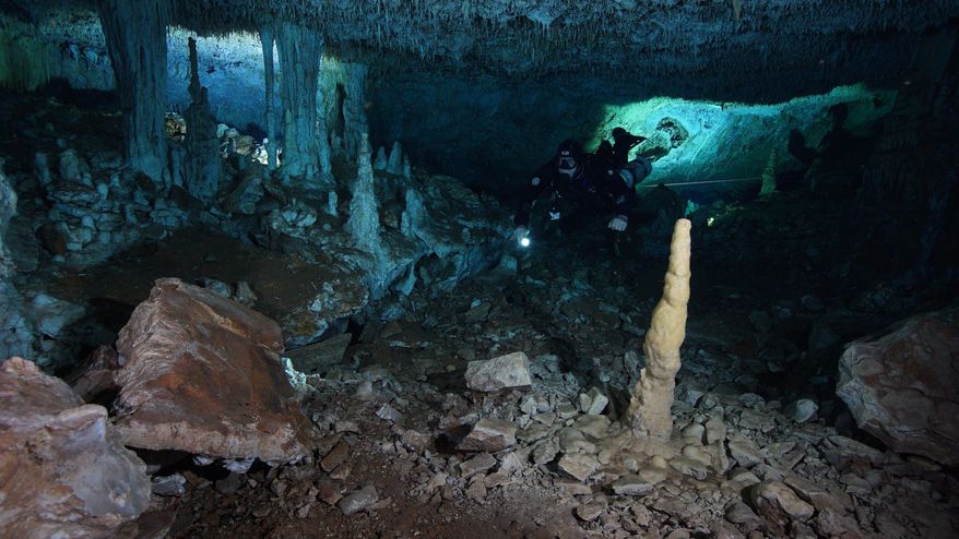 This Dec. 12, 2019 photo released by CINDAQ.ORG, or "Centro Investigador del Sistema Acuífero de Quintana Roo," shows a diver in the "La Mina Roja" passage of the Sagitario underwater cave system near Playa del Carmen in Mexico's Yucatan Peninsula. The discovery of remains of human-set fires, stacked mining debris, simple stone tools, navigational aids, and digging sites suggest humans went into the caves around 12,000 to 14,000 years ago, seeking iron-rich red ocher, which early peoples in the Americas prized for decoration and rituals. (CINDAQ.ORG via AP)