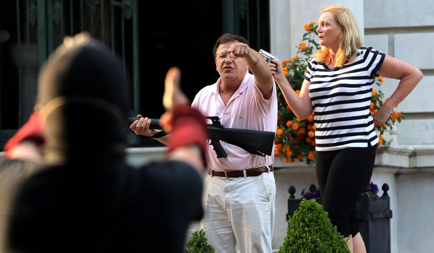 In this June 28, 2020, file photo, armed homeowners Mark and Patricia McCloskey, standing in front their house along Portland Place, confront protesters marching to St. Louis Mayor Lyda Krewson&#39;s house in the Central West End of St. Louis. (Laurie Skrivan/St. Louis Post-Dispatch via AP File)
