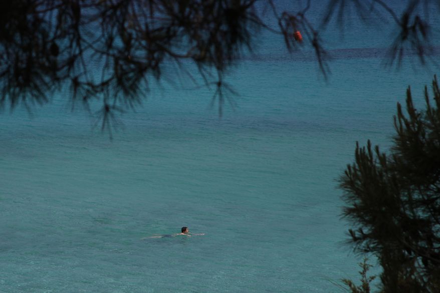 Sunday, May 10, 2020 photo, a lone swimmer wades through the clear waters of &#39;Konnos&#39; beach in Ayia Napa, a seaside resort that&#39;s popular with tourists from Europe and beyond. Cyprus&#39; beleaguered tourism sector got some good news after the government announced on Friday, July 3, 2020, that travelers from the U.K. will be allowed entry into the east Mediterranean island nation next month without having to undergo a compulsory 14-day quarantine. (AP Photo/Petros Karadjias)