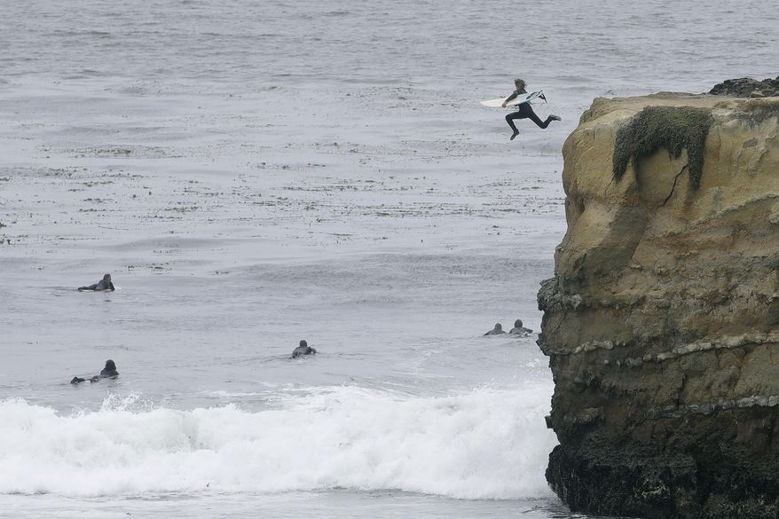 A surfer jumps off a cliff into the water during the coronavirus outbreak in Santa Cruz, Calif., Thursday, July 2, 2020. Californians are being wooed by local tourism boards promising safe and clean lodging, dining and sightseeing in a bid to boost the state&#39;s devastated economy. Visitors bureaus in Sonoma, Santa Cruz, Monterey and greater Palm Springs are among those pitching local travel with messages to wear masks and to practice social distancing. (AP Photo/Jeff Chiu)