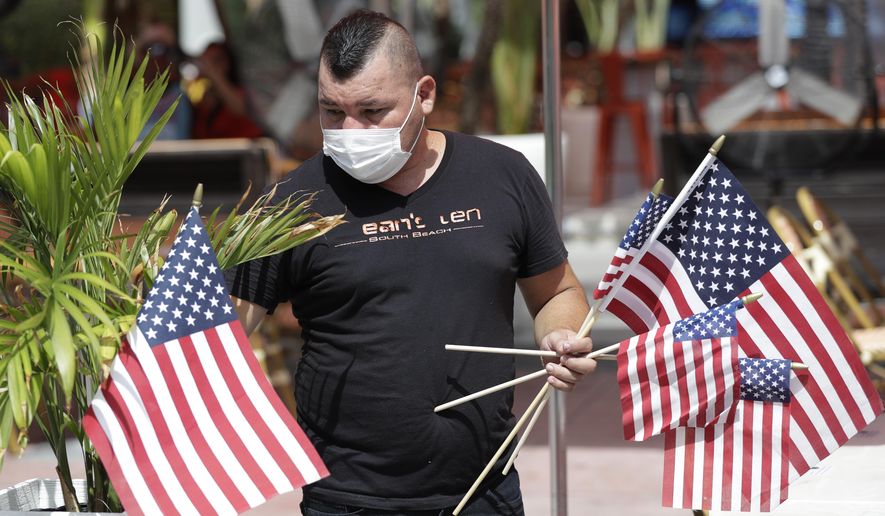 Marvin Turcios puts out American flags at Ocean's 10 restaurant on Miami Beach, Florida's famed Ocean Drive on South Beach, July 4, 2020. The Fourth of July holiday weekend began Saturday with some sobering numbers in the Sunshine State: Florida logged a record number of people testing positive for the coronavirus. (AP Photo/Wilfredo Lee)