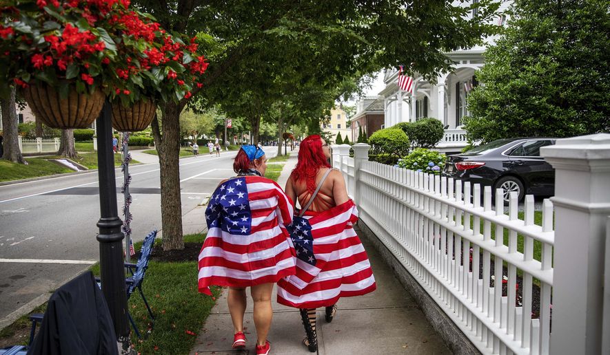 Parade goers draped in American flags walk down the street before a Fourth of July parade begins Saturday, July 4, 2020, in Bristol, R.I. The town, which lays claim to the nation&#39;s oldest Independence Day celebration in the country, held a vehicle-only scaled down version of its annual parade Saturday due to the coronavirus pandemic. (AP Photo/David Goldman)