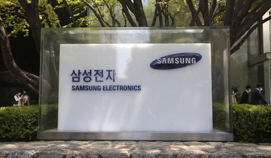 FILE - In this April 28, 2020, file photo, employees walk past a logo of the Samsung Electronics Co. at its office in Seoul, South Korea. Samsung Electronics Co. said Tuesday, July 7, its operating profit for the last quarter likely rose 23% from the same period last year. (AP Photo/Ahn Young-joon, File)