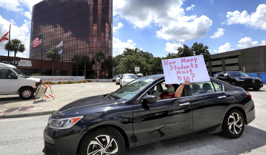 A teacher holds up a sign while driving by the Orange County Public Schools headquarters as educators protest in a car parade around the administration center in downtown Orlando, Fla., Tuesday, July 7, 2020. OCPS teachers are protesting the decision by Gov. Ron DeSantis and the state education commissioner mandating that all public schools open in August despite the spike in coronavirus cases in Florida. (Joe Burbank/Orlando Sentinel via AP) ** FILE **