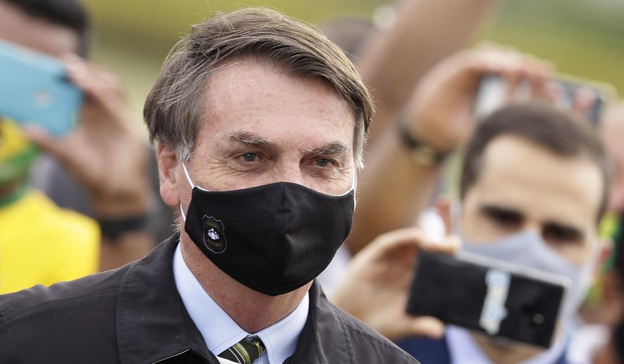 FILE - In this May 25, 2020, file photo, Brazil&#39;s President Jair Bolsonaro, wearing a face mask amid the coronavirus pandemic, stands among supporters as he leaves his official residence of Alvorada palace in Brasilia, Brazil. Bolsonaro said Tuesday, July 7, he tested positive for COVID-19 after months of downplaying the virus&#39;s severity while deaths mounted rapidly inside the country. (AP Photo/Eraldo Peres, File)