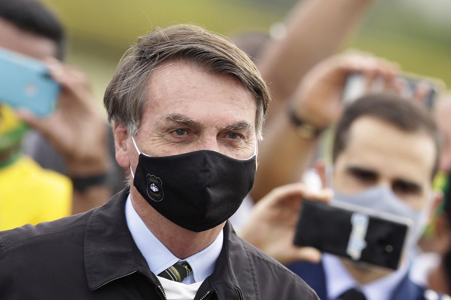 FILE - In this May 25, 2020, file photo, Brazil&#39;s President Jair Bolsonaro, wearing a face mask amid the coronavirus pandemic, stands among supporters as he leaves his official residence of Alvorada palace in Brasilia, Brazil. Bolsonaro said Tuesday, July 7, he tested positive for COVID-19 after months of downplaying the virus&#39;s severity while deaths mounted rapidly inside the country. (AP Photo/Eraldo Peres, File)
