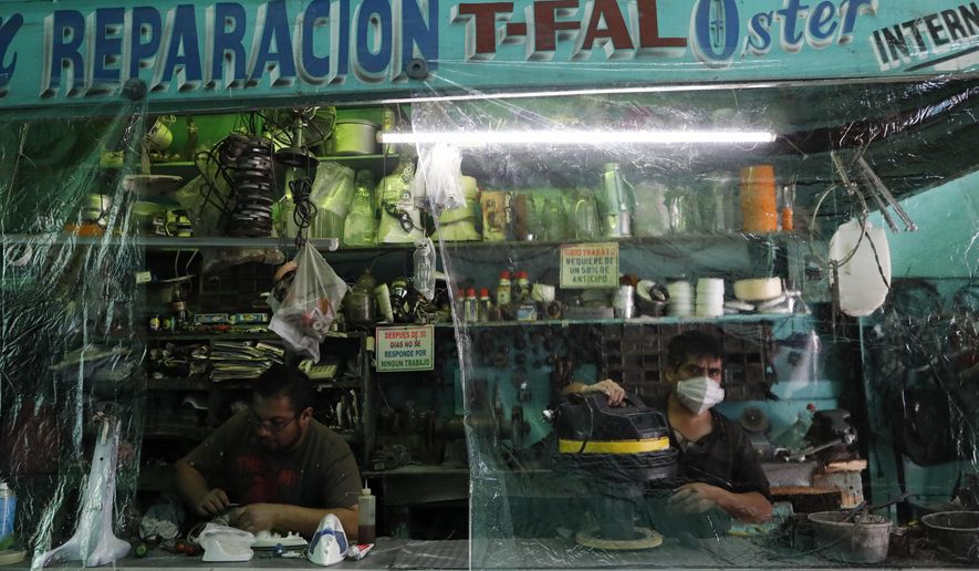 Workers in a small appliance repair shop work behind plastic sheeting to reduce the spread of coronavirus, in central Mexico City, Monday, July 6, 2020. After three months of shutdown, officials allowed a partial reopening of downtown last week, although COVID-19 cases continue to climb. (AP Photo/Rebecca Blackwell)