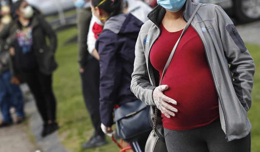 FILE - In this Thursday, May 7, 2020 file photo, a pregnant woman wearing a face mask and gloves holds her belly as she waits in line for groceries with hundreds during a food pantry sponsored by Healthy Waltham for those in need due to the COVID-19 virus outbreak, at St. Mary's Church in Waltham, Mass. A small study in Italy strengthens evidence that pregnant women infected with the coronavirus might be able to spread it to a fetus before birth. Research was released on Thursday, July 9, 2020. (AP Photo/Charles Krupa)