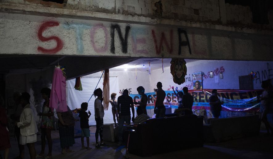 Members of the LGBTQ community gather in the courtyard of the squat known as Casa Nem to watch the weekly presentations by residents on a makeshift stage, in Rio de Janeiro, Brazil, Saturday, May 23, 2020. "Stonewall" is spray painted on an upper beam as a tribute to the Stonewall riots of 1969 in New York, the start of a rebellion that helped propel and transform the modern LGBTQ rights movement. (AP Photo/Silvia Izquierdo)