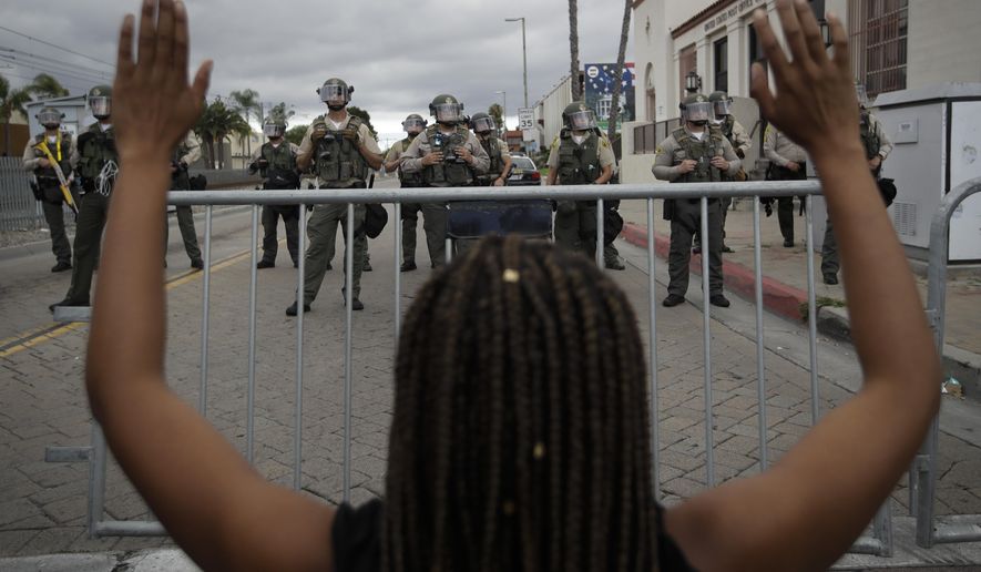 File-A demonstrator raises her arms in the direction of sheriffs during a protest in honor of Andres Guardado Sunday, June 28, 2020, in Compton, Calif. Anti-racism protesters are expected to take to the streets Sunday in a San Francisco Bay Area city where two people were charged with hate crimes after allegedly defacing a city-sanctioned “Black Lives Matter” mural. The two were charged July 7, the same day that police in Martinez, Calif., were called to investigate after someone painted “White Lives Matter” on a city street. (AP Photo/Marcio Jose Sanchez, File)