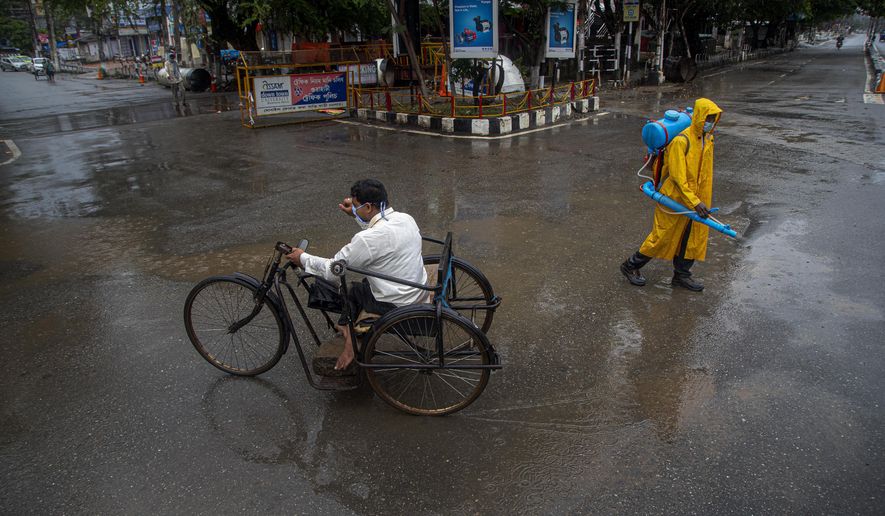 A man rides on a tricycle past a civic worker sanitizing a deserted road during a fresh lockdown imposed in Gauhati, Assam state, India, Sunday, July 12, 2020. India is the world’s third worst-affected country by the coronavirus. (AP Photo/Anupam Nath)