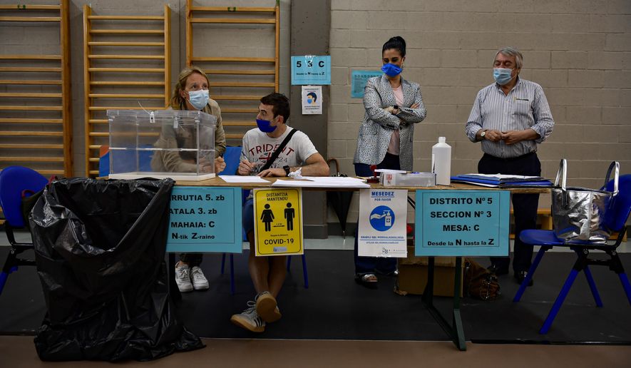 Polling station staff wear face masks to help curb the spread of the coronavirus while waiting for people to vote in the Basque regional election in the village of Durango, northern Spain, Sunday, July 12, 2020. Basque authorities display special rules for protection against the coronavirus. (AP Photo/Alvaro Barrientos)