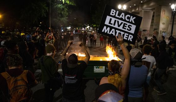 In this Friday, July 10, 2020, file photo, a waste receptacle&#x27;s contents are in flames as protesters gather in downtown Portland, Ore. (Dave Killen/The Oregonian via AP, File)