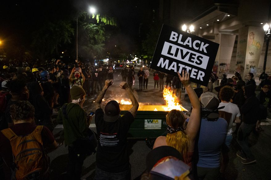 In this Friday, July 10, 2020, file photo, a waste receptacle&#39;s contents are in flames as protesters gather in downtown Portland, Ore. (Dave Killen/The Oregonian via AP, File)