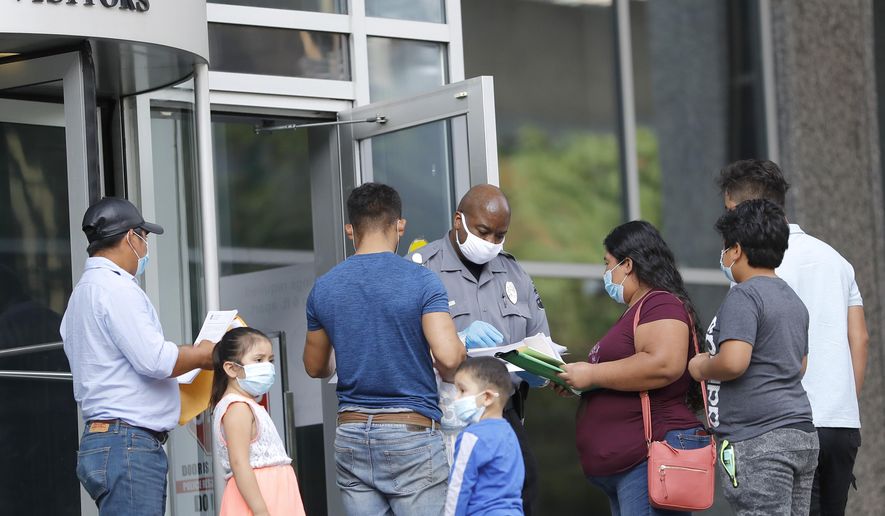 A security officer, center, meets with people outside the federal building to give them a form to return for immigration check-ins at a later date, Monday, July 13, 2020, in Baltimore. Some immigration courts across the country have reopened after closing because of the coronavirus pandemic. (AP Photo/Julio Cortez)