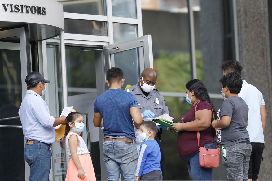 A security officer, center, meets with people outside the federal building to give them a form to return for immigration check-ins at a later date, Monday, July 13, 2020, in Baltimore. Some immigration courts across the country have reopened after closing because of the coronavirus pandemic. (AP Photo/Julio Cortez)